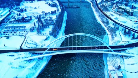 4k-Winter-Aerial-birds-view-over-Walter-Dale-modern-tied-arch-bridge-twist-drift-as-amber-full-length-school-bus-is-midway-crossing-over-North-Saskatchewan-River-reflecting-off-cracked-icy-water2-2