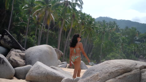 Beautiful-brunette-woman-in-a-bikini-walking-along-a-tropical-rocky-beach---slow-motion