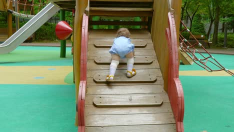 Little-baby-girl-struggling-to-climb-wooden-ladder-at-playground--back-view