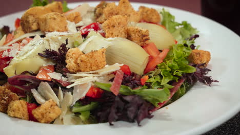 Healthy-nutritious-Italian-side-salad-with-herbed-croutons-artichoke-hearts-and-shaved-parmesan,-slider-close-up-4K