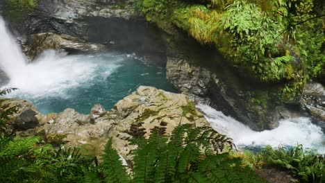 Beautiful-shot-of-lush-waterfall-crashing-down-on-blue-water-pool-and-tropical-stream---Falls-Creek,-Fiordland-national-park