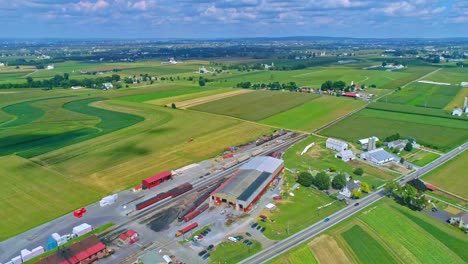 An-Aerial-Traveling-View-of-Corn-Fields-and-Harvesting-Crops,-With-a-Train-Yard-and-Patches-of-Color-on-a-Beautiful-Summer-Day
