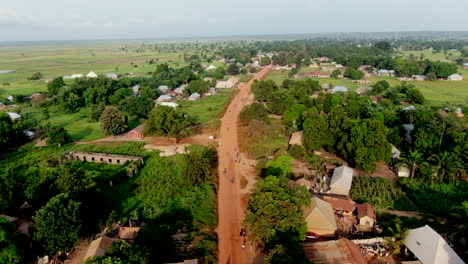 Motorcycle-traffic-along-a-red-dirt-unpaved-road-in-rural-Rukubi,-Nigeria---aerial-flyover