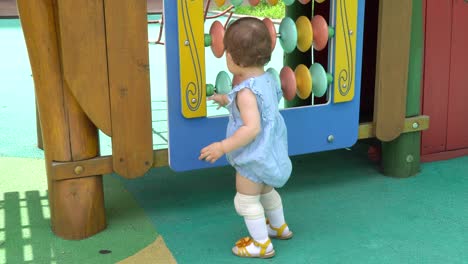 Cute-toddler-at-playground-learning-and-having-fun-spinning-colorful-disks,-Korean-Ukrainian-multi-ethnic-baby-girl