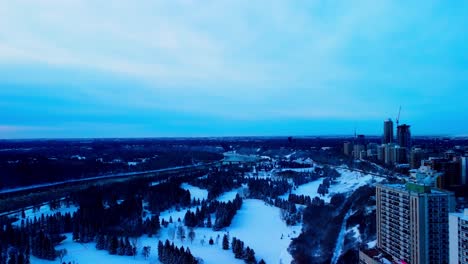 Twilight-4k-Winter-flyover-downtown-valley-Victoria-Park-snow-covered-golf-course-on-the-first-day-of-snow-before-the-City-of-Edmonton-crew-form-the-outdoor-manmade-skating-arena-next-to-road-river