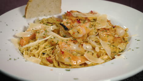 Shrimp-over-angel-hair-pasta-with-focaccia-bread-and-shaved-parmesan-sprinkled-with-herbs-in-white-dish,-slider-4K