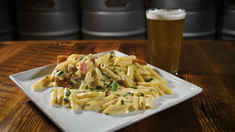 Creamy-chicken-alfredo-with-penne-pasta-and-fried-chicken-breast-paired-with-a-pint-of-beer-at-a-brewery,-slider-4K