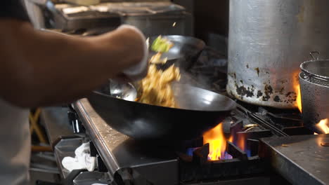 Chef-flips-and-tosses-fried-rice-in-wok-over-flaming-fire-on-commercial-stovetop-in-restaurant-kitchen,-slowmotion-HD