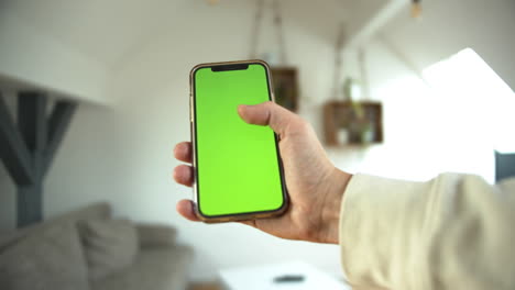 A-man-holding-smartphone-with-greenscreen-tapping-on-the-mobile-in-white-home-background