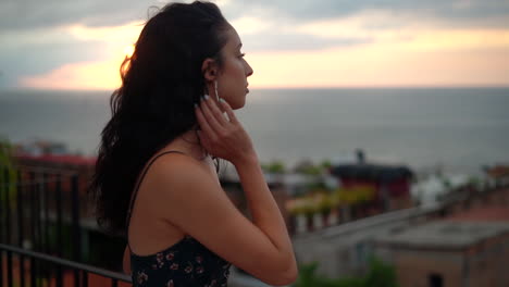 Beautiful-young-woman-on-vacation-takes-in-the-sunset-ocean-and-view-of-the-town-from-the-rooftop