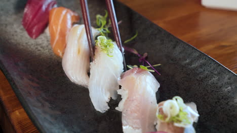 Chopsticks-grab-nigiri-sushi-from-traditional-japanese-sushi-assortment-platter,-close-up-slider-4K