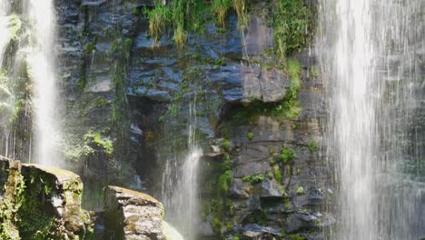 Tilt-down-shot-of-waterfall-crashing-down-rocky-wall-during-sunlight-in-KeriKeri-Waterfalls