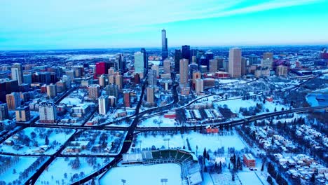 4k-winter1-2-aerial-forward-flyover-Edmonton-Prospects-Baseball-Club,-the-Rossdale-Community-League-Hall-Historic,-the-parking-lot-across-the-street,-and-headed-to-the-snow-covered-downtown-core