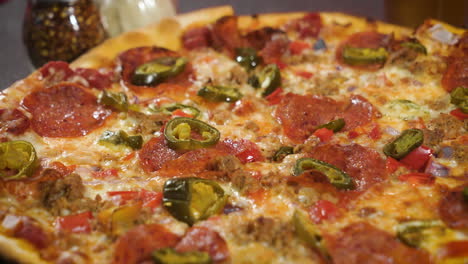 Pizza-De-Pepperoni-Y-Jalapeño-De-Corteza-Fina,-Pizza-Entera-En-La-Mesa-Con-Queso-Rallado-Y-Agitadores-De-Pimienta-Roja,-Cerca-De-4k