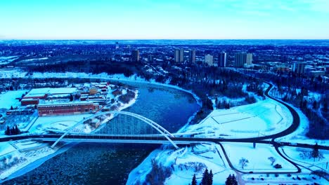 Winter-aerial-forward-flyover-birds-eye-view-dolly-roll-over-the-Walter-Dale-tied-arch-bridge-over-the-North-Saskatchewan-river-in-between-Kinsmen-Park-and-the-Rossdale-Power-Plant-reflective-river3-3