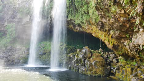 Panning-shot-of-water-from-waterfall-crashing-into-natural-lake-of-dense-jungle---Kerikeri-Waterfalls,NZ-in-Summertime