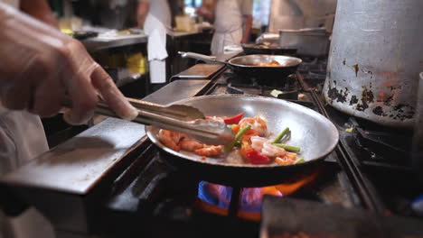 Chef-pan-fries-shrimp-and-vegetables,-cook-uses-tongs-to-move-around-vegetables-and-shrimp-in-pan,-slow-motion-HD