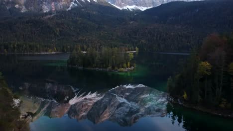 Sunset-drone-flight-over-Eibsee,-while-Zugspitze-is-reflecting-in-the-lake,-surrounded-by-autumnal-trees