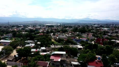 Aerial-view-of-the-suburbs-of-the-city-of-city-of-Oaxaca-in-Mexico,-filmed-by-a-drone-with-vertical-displacement-and-mountains-in-the-background