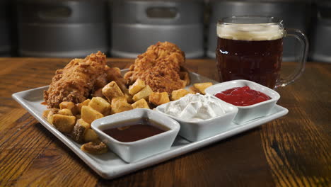 Fried-chicken-tenders-and-home-fries-with-a-trio-of-dipping-sauces-paired-with-a-dark-lager,-slider-4K