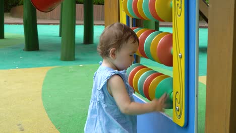 2-years-old-Ukrainian-Korean-Cute-toddler-girl-learning-and-having-fun-spinning-colorful-disks-at-playground,-Korean-Ukrainian-multi-ethnic-baby-girl