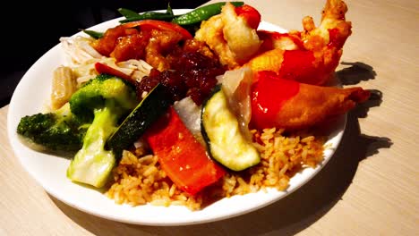 Chinese-Food-Plate-Piled-with-popular-favorites-of-deep-fried-breaded-chicken-balls-n-prawn-shrimps-with-baby-corn-bean-sprouts-soy-beans-sliced-zucchini-fried-rice-sliced-peppers-rotating-plate-table