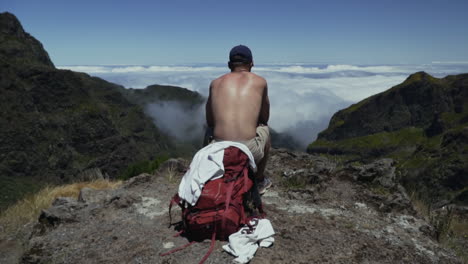 Young-man-takes-break-on-scenic-overlook-above-cloud-filled-valley,-slow-motion