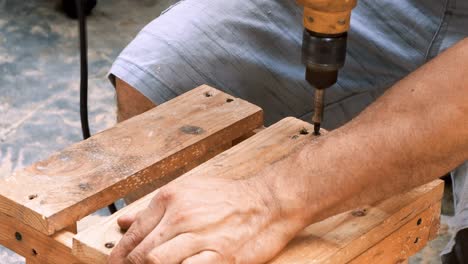 Skillfull-carpenter-employing-a-power-drill-to-attaching-screws-into-a-small-wooden-chair-in-his-small-business-workshop-to-sell-and-support-the-local-economy