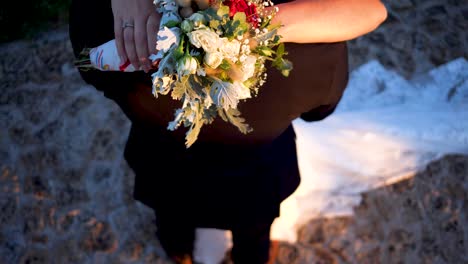 wedding-couple-holding-arms-with-beautiful-flower-bouquet,-top-down-shot
