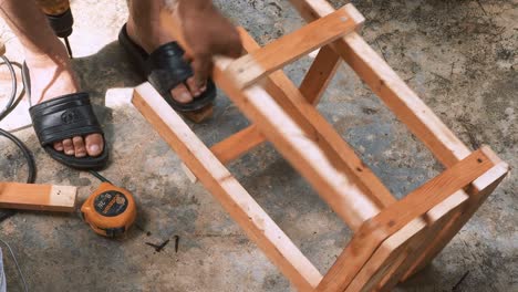 Skillfull-carpenter-employing-a-power-drill-to-attaching-screws-into-a-small-wooden-chair-in-his-small-business-workshop-to-sell-and-support-the-local-economy