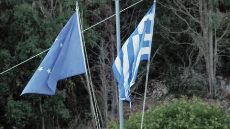 Bandera-De-La-Unión-Europea-Y-Bandera-Griega-Moviéndose-Soplada-Por-El-Viento-En-La-Isla-De-Kefalonia,-Grecia