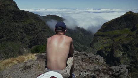 Young-man-sits-on-overlook-and-takes-in-dramatic-view-of-cloud-covered-valley
