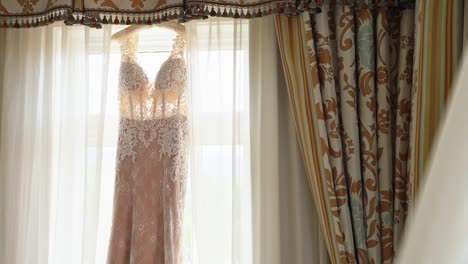 Fleischrosa-Hochzeitskleid,-Das-An-Einem-Hellen-Fenster-Mit-Weißem-Vorhang-Und-Dekorativen-Vorhängen-Hängt