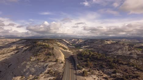 Drone-shot-flying-over-All-American-Road-state-route-scenic-byway-12-with-a-white-car-passing-in-the-Grand-Staircase-Escalante-National-Monument-in-Utah,-USA-in-4k