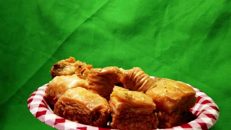 4k-Loop2-3-rotating-plate-of-baklava-on-an-appetizer-plate-with-a-green-screen-background-and-all-the-desserts-vary-in-squares,-rolls-with-pistachio-inside-and-glazed-with-rose-water-sugar-to-reflect
