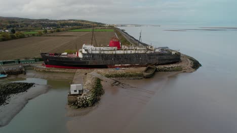 Derelict-remains-of-liner-ship-docked-on-sandy-coast,-aerial-orbit-view