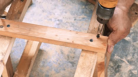 Traditioneller-Zimmermann,-Der-Eine-Mannschaft-In-Ein-Stück-Holz-Bohrt,-Um-Die-Beine-Eines-Stuhls-Zu-Bauen,-Der-Als-Möbel-Verkauft-Wird
