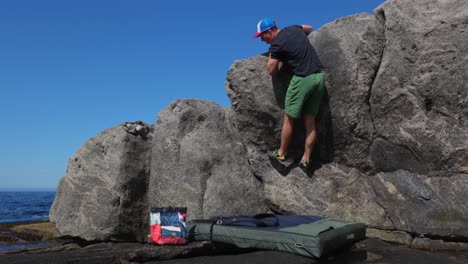 Young-man-bouldering-on-rocky-beach-with-sea-in-background