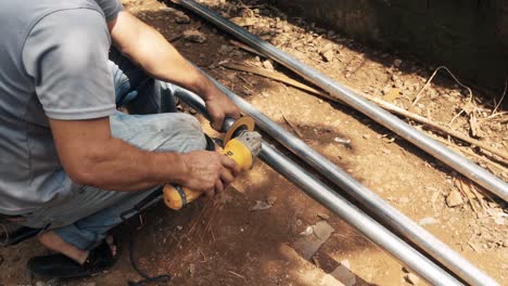 Man-cutting-a-galvanized-steel-tube-with-an-industrial-electric-angle-grinder-to-elaborate-a-metal-structure-in-a-rural-environment-construction-site-worplace