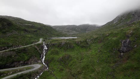 Flying-towards-waterfall-and-lake-next-to-small-road-in-a-narrow-valley-on-Senja-in-Norway