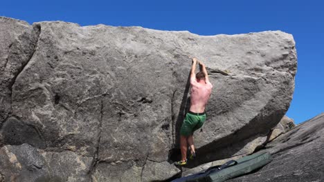 Young-man-bouldering-on-rock-without-shirt-with-sunny-weather-at-rocky-beach