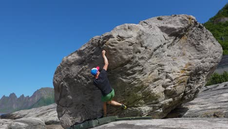 Young-man-bouldering-on-rock-on-Senja-in-norway-with-good-weather-and-mountains-in-the-background