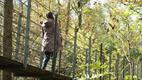 Pretty-girl-in-a-purple-warm-cozy-jacket-walks-across-a-suspension-bridge-during-the-autumn-season-and-explores-in-wonder
