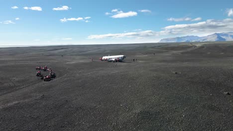 Group-ot-tourist-on-quad-bikes-exploring-crashed-plane-of-Iceland,-aerial-view