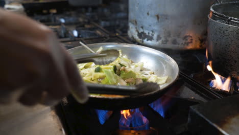 Chef-uses-tongs-to-stir-fry-fresh-vegetables-over-flames-on-commercial-restaurant-kitchen-stove,-slow-motion-HD