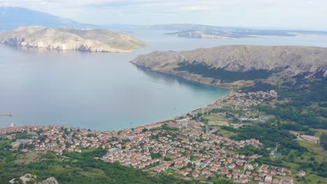 Aerial-arc-shot-high-above-the-town-of-Baska-on-Krk-Island,-Croatia-looking-out-to-sea