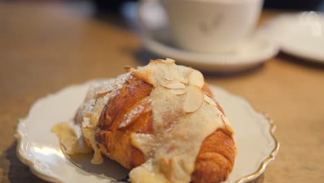 Primer-Plano-De-Un-Sabroso-Croissant-De-Estilo-Sueco-Cubierto-Con-Almendras-En-Un-Restaurante-Tradicional