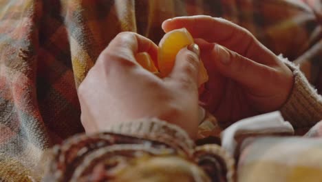 Woman-eating-a-tangerine-in-a-close-up-shot-in-a-warm-interior-environment-with-tartan-plaid