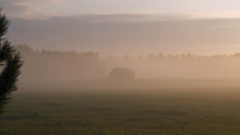 Silhouette-of-old-barn-hiding-in-foggy-early-morning,-distance-view