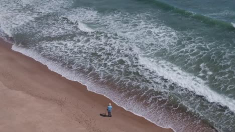 Drone-Pan-Over-Male-Fisherman-Adjusting-Fishing-Rod-on-Rough-Cape-Cod-Shoreline